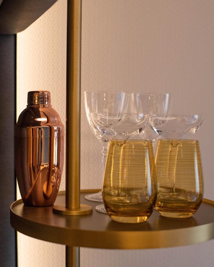 Middle Eight - Covent Garden - Preferred Hotels And Resorts London Exterior photo The photo shows a stylish bar setup featuring a shiny copper cocktail shaker positioned next to several elegant glassware pieces. There are four tall, clear stemmed glasses and two round, amber-colored glasses with a textured pattern. The background 