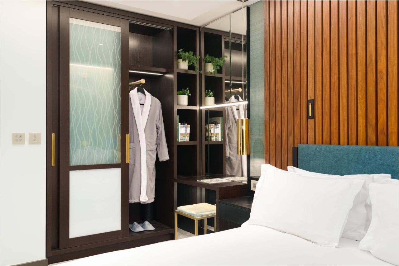 Middle Eight - Covent Garden - Preferred Hotels And Resorts London Exterior photo The photo shows a cozy hotel room featuring a neatly made bed with white bedding. On the side, there is a wardrobe with sliding glass doors. Inside the wardrobe, a light-colored robe is hanging, and there are shelves with small plants and toiletries 