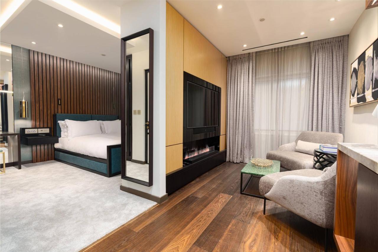 Middle Eight - Covent Garden - Preferred Hotels And Resorts London Exterior photo The photo depicts a modern hotel room or suite featuring a cozy living space. On one side, there's a comfortable bed with plush bedding, positioned against a backdrop of elegant wooden paneling. Adjacent to the bed is a contemporary fireplace integra