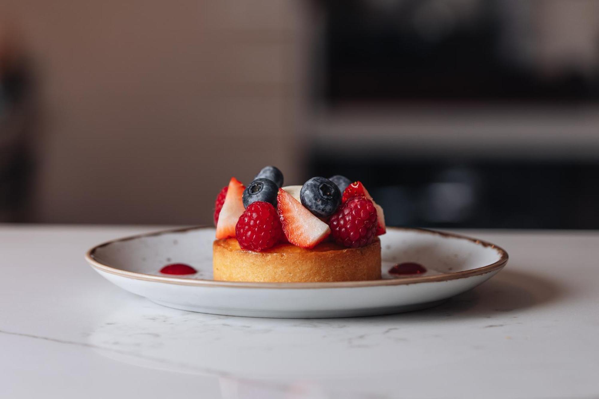 Middle Eight - Covent Garden - Preferred Hotels And Resorts London Exterior photo The photo shows a delicious-looking dessert on a white plate. The dessert appears to be a small tart or cake topped with fresh strawberries, raspberries, and blueberries. It has a golden crust, and there are small dollops of a red sauce or fruit pure