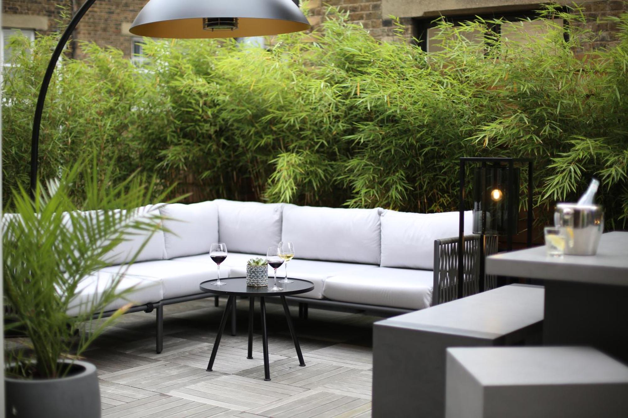 Middle Eight - Covent Garden - Preferred Hotels And Resorts London Exterior photo The photo shows an outdoor seating area featuring a modern gray sectional sofa with plush cushions. In front of the sofa is a small, round black table with two glasses of wine on it, accompanied by a decorative plant or vase. Surrounding the area are